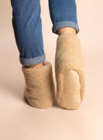 wysokie beżowe kapcie z wełny na stopach, dżinsy z podwiniętymi nogawkami, neutralne tło