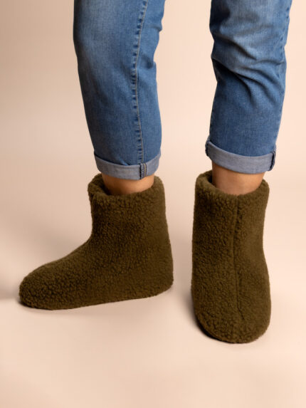 hohe khakifarbene Wollhausschuhe an den Füßen, sichtbare Jeans, neutraler Hintergrund