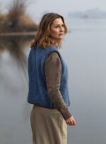 Kobieta w niebieskiej kamizelce wełnianej stoi nad wodą w naturalnym otoczeniu