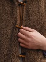 brązowa wełniana kurtka z drewnianymi zapięciami i ręką trzymającą zapięcie