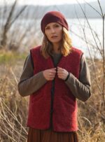 Kobieta w czerwonym kamizelce wełnianej i brązowym swetrze, w tle naturalny krajobraz