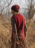 Kobieta w czerwonej kamizelce i brązowej spódnicy, stojąca wśród suchych traw