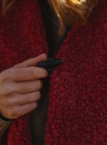 czerwona wełniana kamizelka i dłoń trzymająca jej czarny guzik