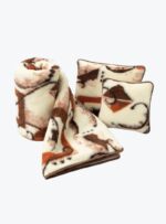 wełniany koc w odcieniach beżu i brązu oraz dwie poduszki z tym samym wzorem na neutralnym tle