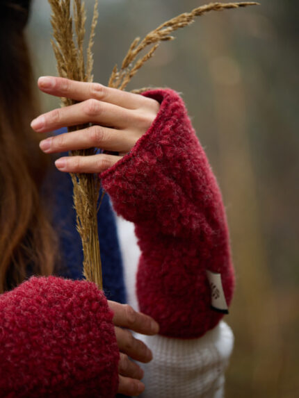 Ręce w czerwonych mitenkach z wełny trzymają suche źdźbła trawy w otoczeniu przyrody