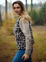 Kobieta w kamizelce wełnianej w panterkę stoi w lesie otoczona drzewami i trawą