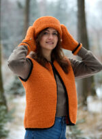 Kobieta w pomarańczowej kamizelce i opasce w lesie zimą, trzyma ręce na głowie