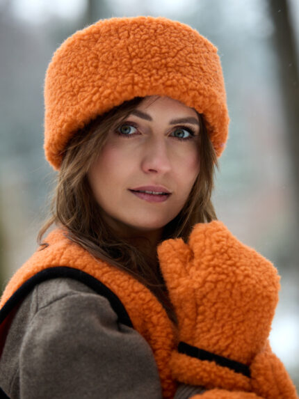 Kobieta w pomarańczowej opascei rękawiczkach i kamizelce w zimowym otoczeniu