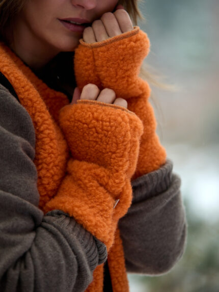Kobieta w pomarańczowej, wełnianej kamizelce z rękawiczkami bez palców w zimowym otoczeniu