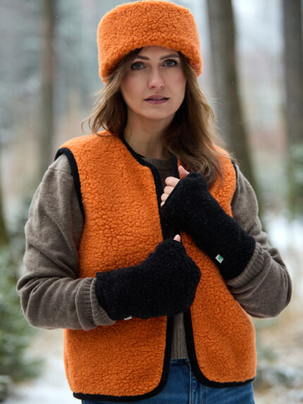 Kobieta w pomarańczowej kamizelce i czarnych rękawicach, w tle las pokryty śniegiem