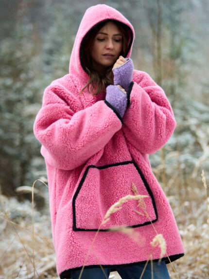 Kobieta w różowej bluzie wełnianej z kapturem stoi na tle lasu