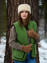 Kobieta w zielonej kamizelce i brązowych rękawiczkach stoi przy drzewie w lesie