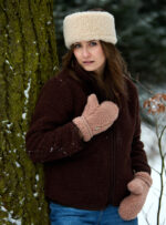 Kobieta w bordowej kurtce wełnianej i beżowych rękawicach stoi przy drzewie w lesie. Zimowa aura.