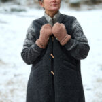 Kobieta w szarym płaszczu z wełny i brązowych rękawiczkach, zimowy krajobraz w tle