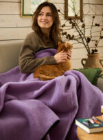 Kobieta w brązowym swetrze trzyma kota na liliowym kocu wełnianym w przytulnym wnętrzu