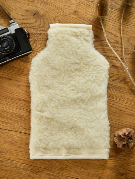 Pokrowiec ecru z wełny na termofor na drewnianym stole obok aparatu fotograficznego