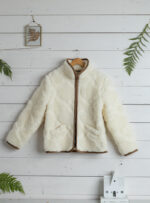 kurtka w kolorze białym z brązowym wykończeniem zawieszona na tle białych desek