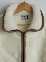 biała kurtka z wełny z brązowymi detalami na wieszaku