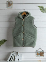 Szałwiowa kamizelka damska z kieszenią i zapięciem na sznurku na tle jasnych desek i dekoracji.