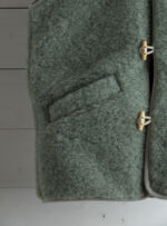 Szałwiowa kamizelka damska z kieszenią i zapięciem na sznurku na tle jasnych desek