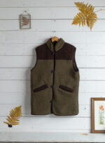 Kamizelka khaki z brązowymi detalami powieszona na wieszaku na tle białych desek