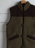 kamizelka khaki z brązowymi detalami na tle białej ściany