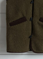 kamizelka khaki wełny z brązowymi detalami na tle jasnego drewna