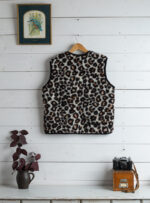 kamizelka w cętki pantery na wieszaku, obok doniczka z rośliną i stara kamera na stoliku