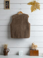 Tył brązowej kamizelki z wełny na wieszaku w jasnym wnętrzu z dekoracjami