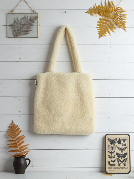 Jasna torba na zakupy z wełny zawieszona na białej ścianie w otoczeniu roślin i dekoracji
