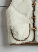 wełniana kamizelka w kolorze ecru z brązowymi detalami na tle jasnego drewna