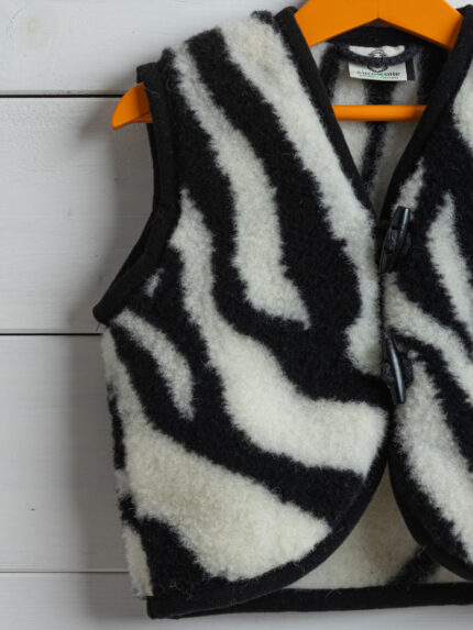 kamizelka z wełny ze wzorem zebry na wieszaku w tle białe deski