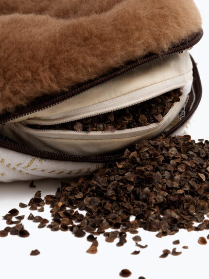 brązowa poduszka z wełny z otwartym zamkiem błyskawicznym, z nasionami rozsypanymi obok na białym tle