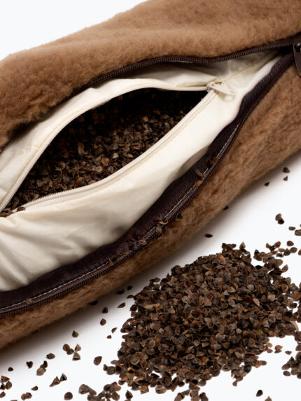 brązowa poduszka z wełny z widocznym zamkiem i rozsypanymi łuskami gryki obok