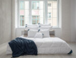 Biała kołdra na łóżku z granatowym kocem i poduszkami w jasnym wnętrzu