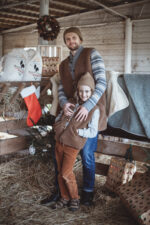 Mężczyzna i dziecko w brązowych kamizelkach w stajni, w tle choinka i prezenty