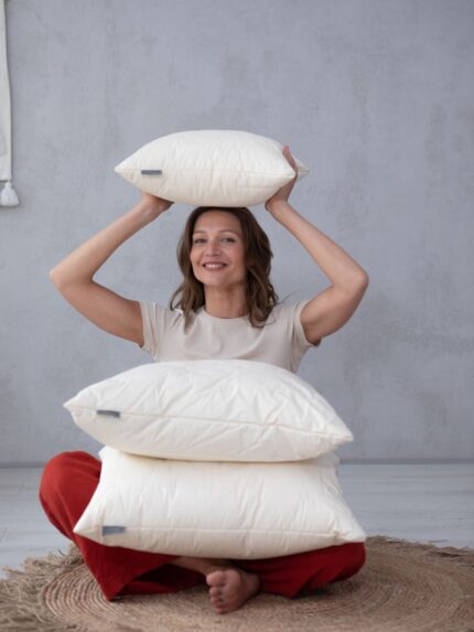 Poduszka z wełny merino w naturalnym kolorze, model prezentowany przez kobietę w jasnym wnętrzu.