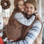 Dziecko w brązowej kamizelce na ramionach mężczyzny w ciepłej odzieży w drewnianym wnętrzu