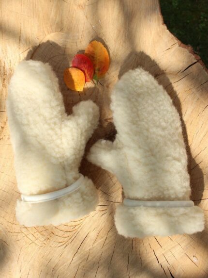 rękawice wełniane ecru na tle drewnianego stołu z kolorowymi liśćmi