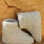 wełniane kapcie w jasnym kolorze na tle drewnianego plastra