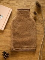 Brązowy pokrowiec do termoforu z wełny na drewnianym blacie obok notesu i suchych roślin