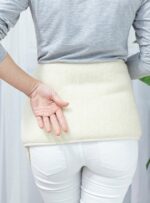 Kobieta w szarym swetrze z białym pasem wełnianym trzyma rękę za plecami w jasnym wnętrzu