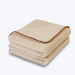 Złożony koc z wełny alpaki w kolorze ecru z brązowym obszyciem, na neutralnym tle.