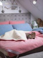 Kołdra wełniana w kolorze różowym i białym z leżącym kotem na łóżku z poduszkami