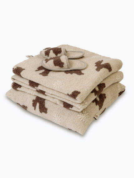 beżowy koc i poduszka z brązowym wzorem i kapcie na neutralnym tle