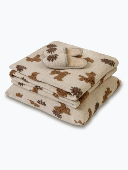 beżowa kołdra i poduszka z brązowymi wzorami i szare kapcie na neutralnym tle