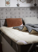 Poduszki na łóżku z szarym zagłówkiem, na ochraniaczu z wełny w kolorze ecru