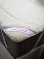 beżowy ochraniacz na materac z wełny na ciemnym materacu