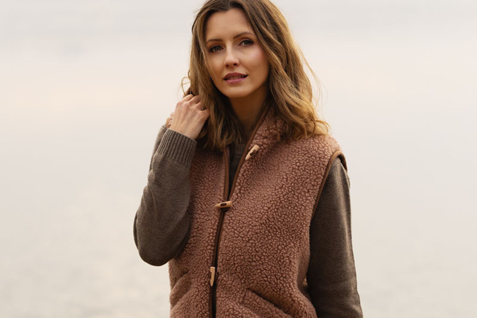 Kobieta w brązowej kamizelce z wełny dotyka włosów. Mgliste tło