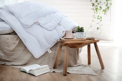 białe kołdry na łóżku, książką i filiżanką na drewnianym stoliku w jasnym wnętrzu
